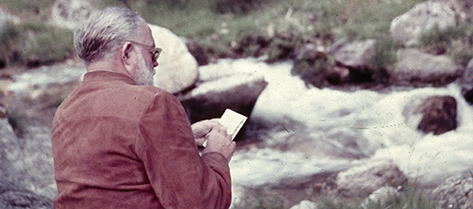 Ernest Hemingway sitting near a stream and writing, near San Ildefonso, Spain. 1959